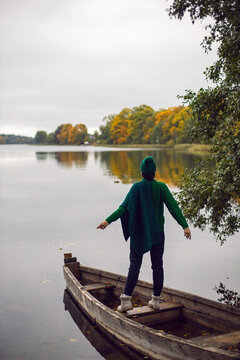 woman in a green sweater, hat and sunglasses stands on an old wooden boat by the lake in autumn in the village. Vertical.