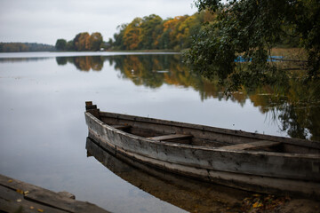 Naklejka na ściany i meble old wooden fishing boat stands on the lake in the village of autumn in cloudy weather.