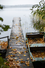 old wooden fishing green boat stands at the pier on the lake in the village of autumn in cloudy weather.