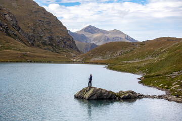 Fototapeta na wymiar The girl stands on a stone against the backdrop of mountain peaks and a blue turquoise lake. Beautiful mountain landscape for recreation, travel and a healthy lifestyle. Caucasus, Russia