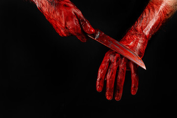 A man wipes a bloody knife with his hand on a black background.  - obrazy, fototapety, plakaty