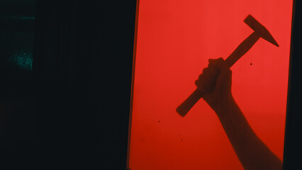 Silhouette of a hand holding a hammer behind a glass door and red background