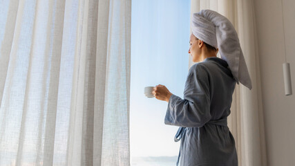 Relaxed woman wearing bath robe drinking coffee in hotel room in morning