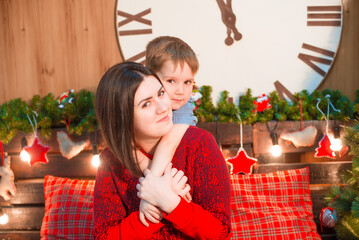 
A young mother with dark hair and a son by the Christmas tree in a room decorated for Christmas. Family Christmas. Christmas mood