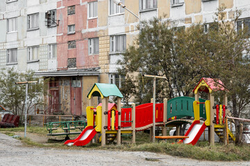 Fototapeta na wymiar Multi-colored children's playground in the city courtyard near the old panel building. Problems of improvement of old urban quarters in the province. There is no one on the street.