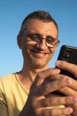 an adult man holding a smartphone in his hands looks there and smiles, the background is the sky