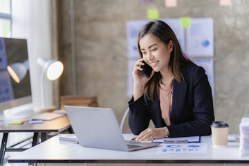 Asian businesswoman holding smartphone with charts or documents at work using business laptop calculator financial accountant calculating money