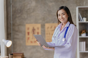 Asian female doctor sitting at a hospital desk, giving health care and disease prevention advice, convenient online services to patients and smiling, writing prescriptions to order medicine.