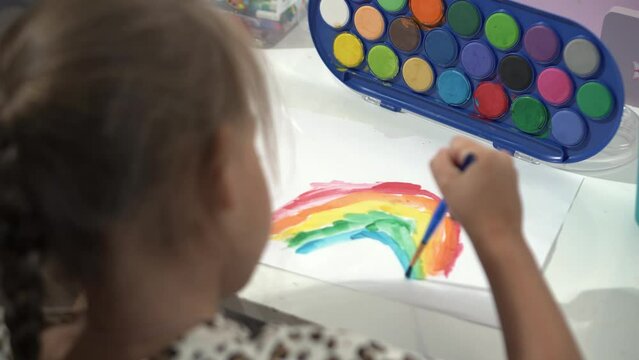 Talented Creative Child Girl Female Artist Draws Rainbow sky summer on Paper, Using Fingers Paints Brush Creates Colorful, Kid Drawing on table at Home. Painter Creating Abstract Modern Art. Childhood