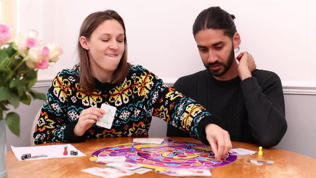 South Asian man playing board game with young white woman who is smug after her move