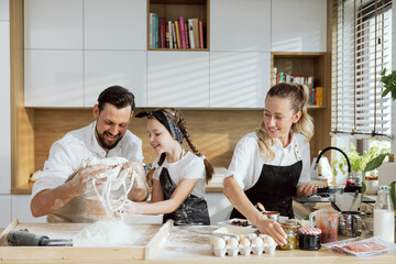 Adorable family in modern kitchen coking baking together. Happy father pouring flour delighted...