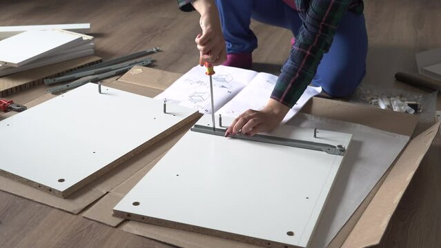 Woman screwing screw while assembling furniture on the floor of apartment