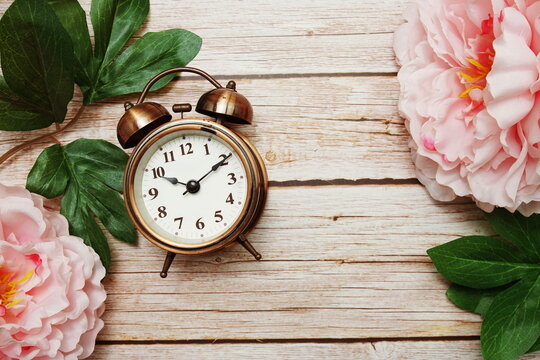 Alarm clock with pink peony flowers border frame on wooden background