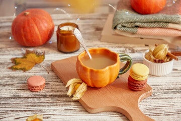 Aesthetics seasonal pumpkin latte in cup shape of pumpkin. Lagom lifestyle, colorful pumpkins, macaroons and leaves. Cozy autumn home