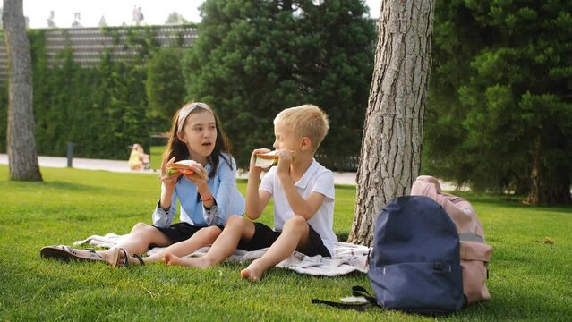 Elementary school students boys and a girl sat down together under a tree for lunch with sandwiches.