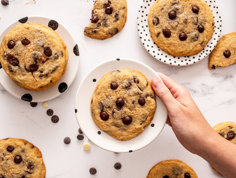 Chocolate chip cookies on polka dots plates with a young female hand holding its top view, horizontal image