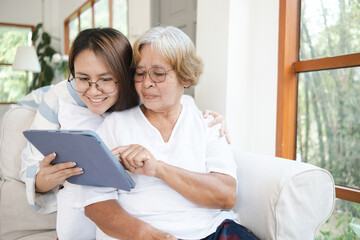 Fototapeta premium Asian caregiver and senior woman using digital tablet at home, fostering technology literacy and intergenerational connection