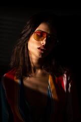 Fototapeta premium Closeup image of a young brunette woman in colorful clothes and sunglasses, dark background.