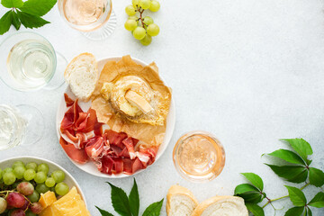 Top view of table with rose and white wine in glasses, plates with grapes, cheese and jamon, baked...