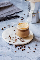 Ice cold coffee brew in a Moka pot on a marble round tray on a blue table with some coffee beans spread around, a close-up cold drink