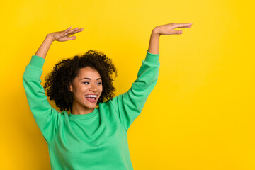 Portrait of overjoyed chilling person raise hands make moves look empty space isolated on yellow...