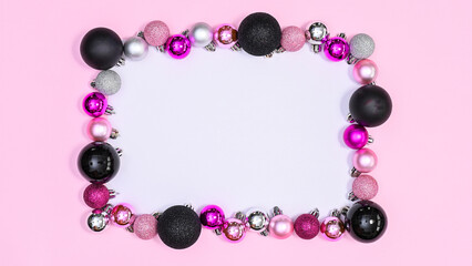 White copy space paper surrounded with silver, black and pink shiny Christmas ornamnets on pastel pink background. Flat lay