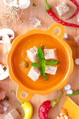 Autumn hot pumpkin soup with croutons and mint in pumpkin shaped bowl surrounded by green and red peppers, mushrooms, garlic. flat lay food photo