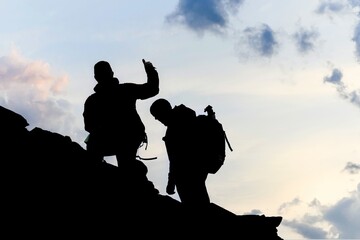 Anonymous climbers silhouetted by dramatic sky climbing mountain face with thumbs up.
