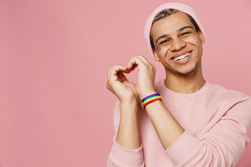 Young smiling happy fun gay man wear sweatshirt hat showing shape heart with hands heart-shape sign isolated on plain pastel light pink color background studio portrait. Lifestyle lgbtq pride concept. - obrazy, fototapety, plakaty