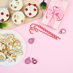Christmas cup cakes, gingerbread cookies and candy canes on pastel pink background with copy space. Flat lay