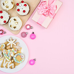 Sweet gingerbread cookes and cup cakes with Christmas ornaments on pastel pink background. Flat lay