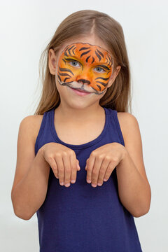 Waist up of smiling caucasian girl of six years looking at camera on white background with tiger face painting holding hands like paws