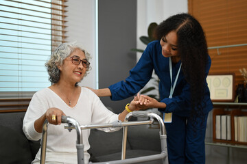Friendly female caregiver helping elderly woman with walking frame at home. Home health care service concept