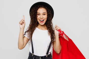 Young woman 20s wear t-shirt hat hold in hand red paper package bags after shopping point index...