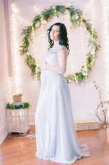 Young pregnant woman with dark hair in airy dress in a room decorated with pine needles and sparkling garlands for Christmas. Christmas mood . Pregnancy