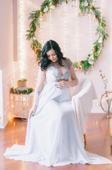 Young pregnant woman with dark hair in airy dress in a room decorated with pine needles and sparkling garlands for Christmas. Christmas mood . Pregnancy