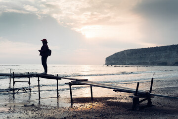 Traveller's silhouette on an old wooden pier at Zapallo Bay (Apollo bay). Episkopi, Limassol District, Cyprus