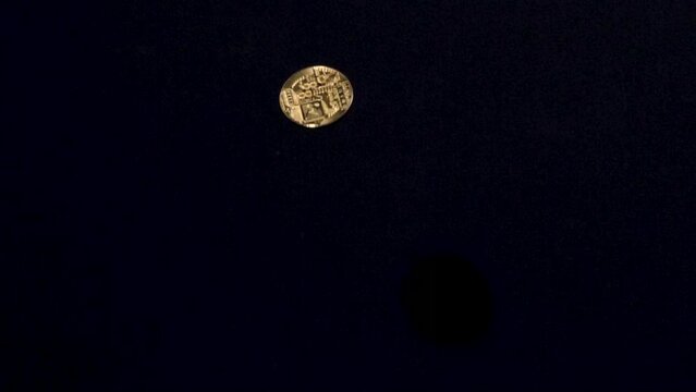 Gold bitcoin coin flipping in the air in slow motion against black background.