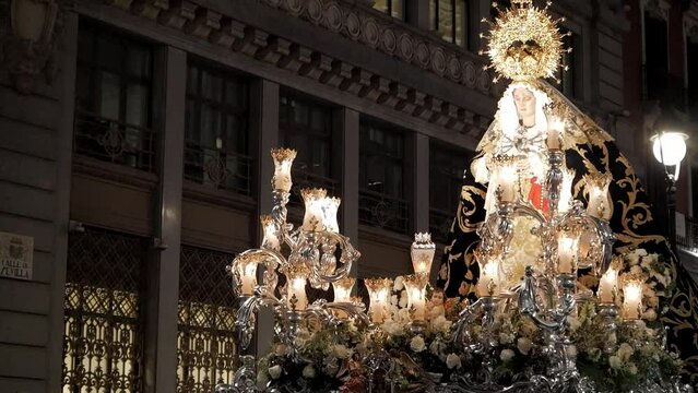 Virgin Mary procession on Good Friday during Holy Week celebrations in Madrid, Spain. Float has a figure of Virgin Mary surrounded by lantern. She wears a tunic and has a golden crown around her.