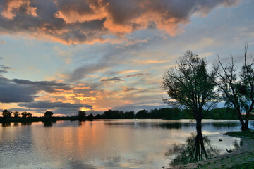 Obraz premium sunset over the lake in the meadow with reflection in the water of the sky with clouds, trees, ducks, fisherman
