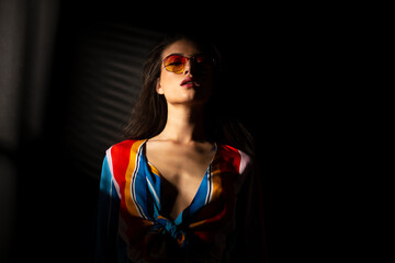 Portrait of a young brunette young woman in colorful clothes and sunglasses, with closed eyes. Space for text.