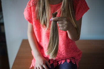 Hair donation. Girl holding her long cut off natural blond ponytail hair tied together.  - obrazy, fototapety, plakaty