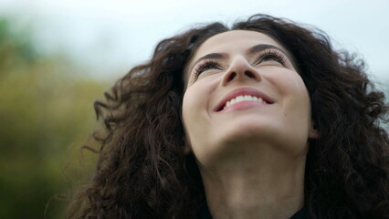 Young woman looking up at sky with HOPE. Contemplative 30s girl standing outdoors raises looks up smiling