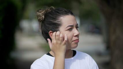 Thoughtful casual young woman standing outside in contemplation. Pensive 20s girl adjusting hair