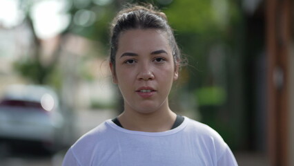 Portrait of a serious casual hispanic girl. Young woman in 20s standing outdoors in city street...
