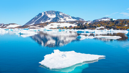 Naklejka premium Panoramic view of colorful Kulusuk village in East Greenland - Kulusuk, Greenland - Melting of a iceberg and pouring water into the sea - Drummer statue in the foreground