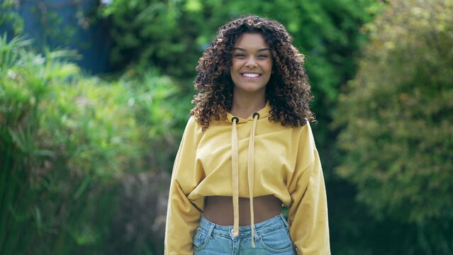 One Trendy Happy African American Girl With Curly Hair And Yellow Blouse Standing Outdoors. A Smiling Black Hispanic Latina 20s Woman In Vertical Video