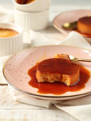 Creme caramel on pink plates on a white wooden table, with a golden spoon