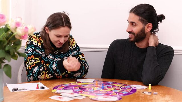 South Asian man playing board game with young white woman who is smug after her move