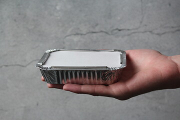 Hand holding disposable food container kitchen tray, aluminum foil isolated on gray rusticoo, front...